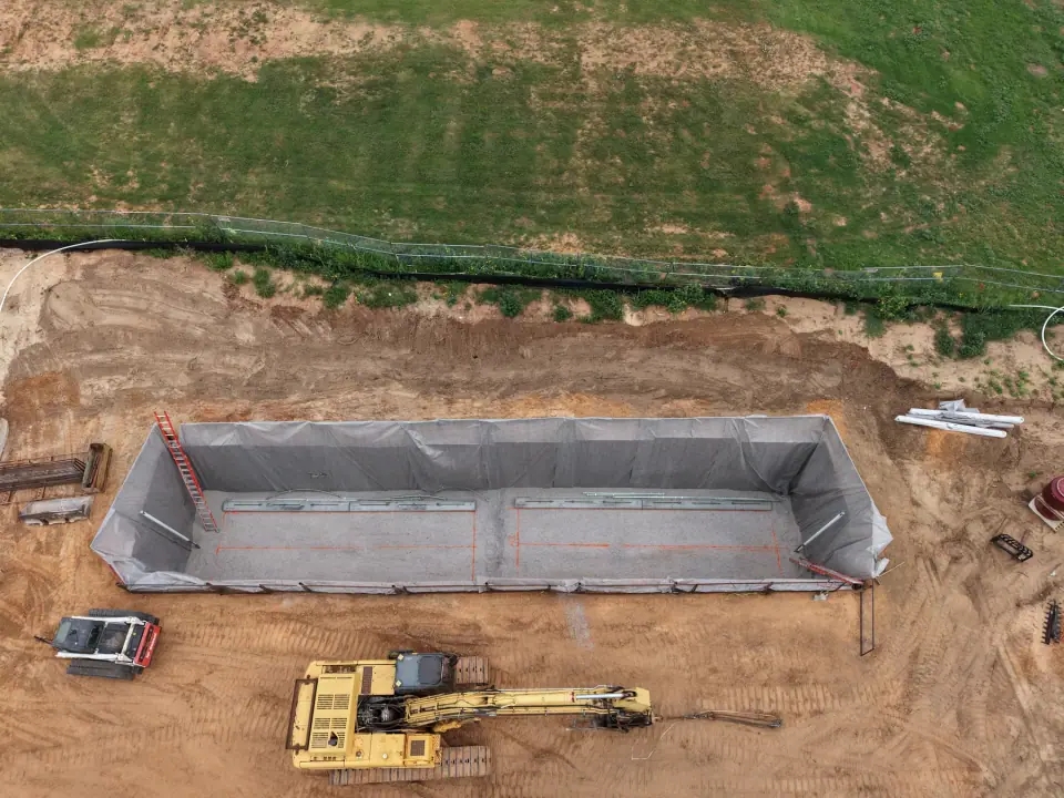 Lined excavation with an excavator ready to set the tanks
