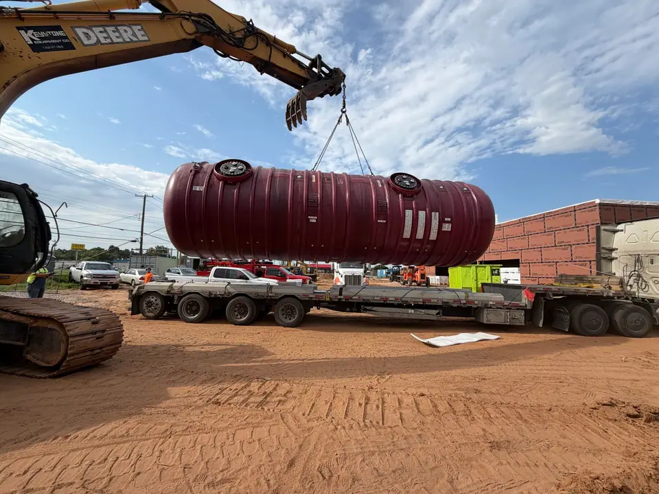 Excavator unloading a double-wall fiberglass tank from the delivery trailer