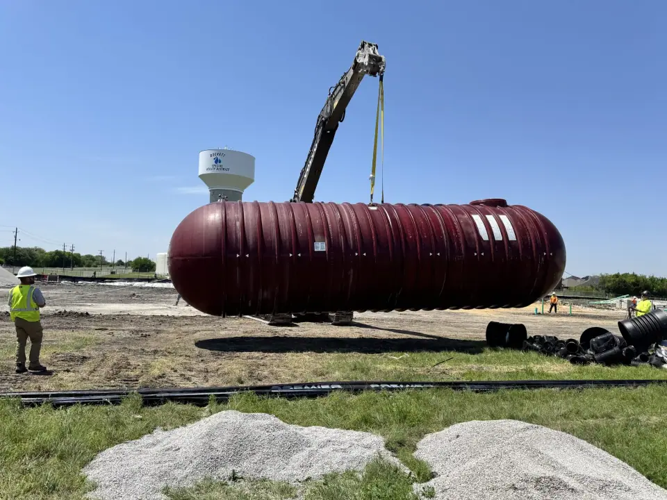 Tank lifted by excavator with the water tower in the background